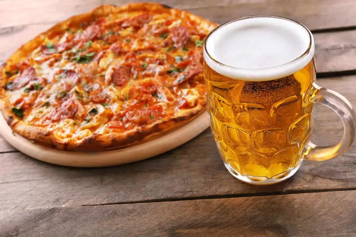 A glass of craft beer next to a slice of pizza.