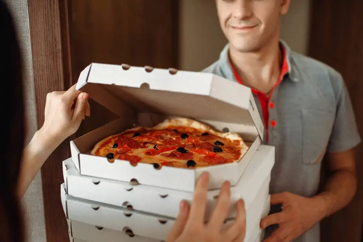 A pizza box being handed to a customer.