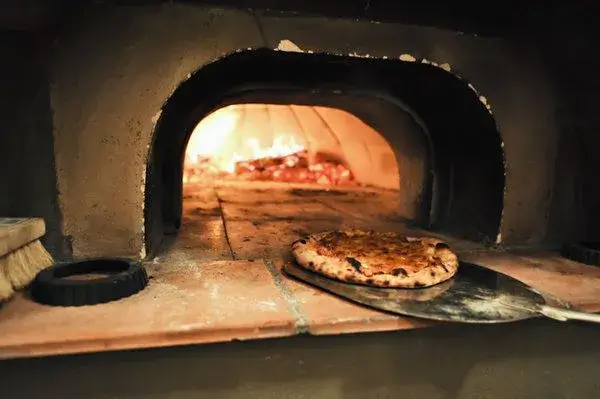 A pizza being taken out of a brick oven