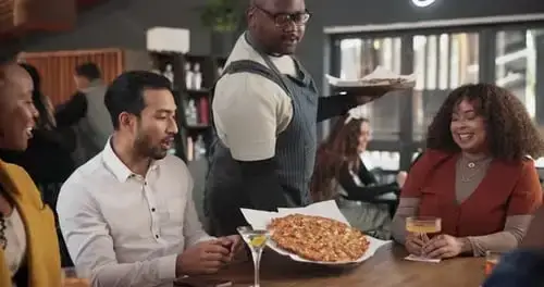 Friends laughing and sharing a pizza in a cozy restaurant.